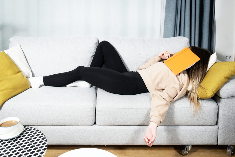 Teen fell asleep on couch with book on face.