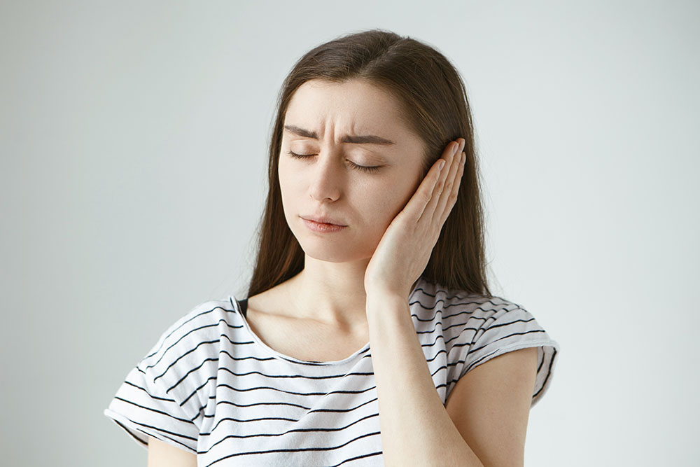 A woman is holding her ear in pain.