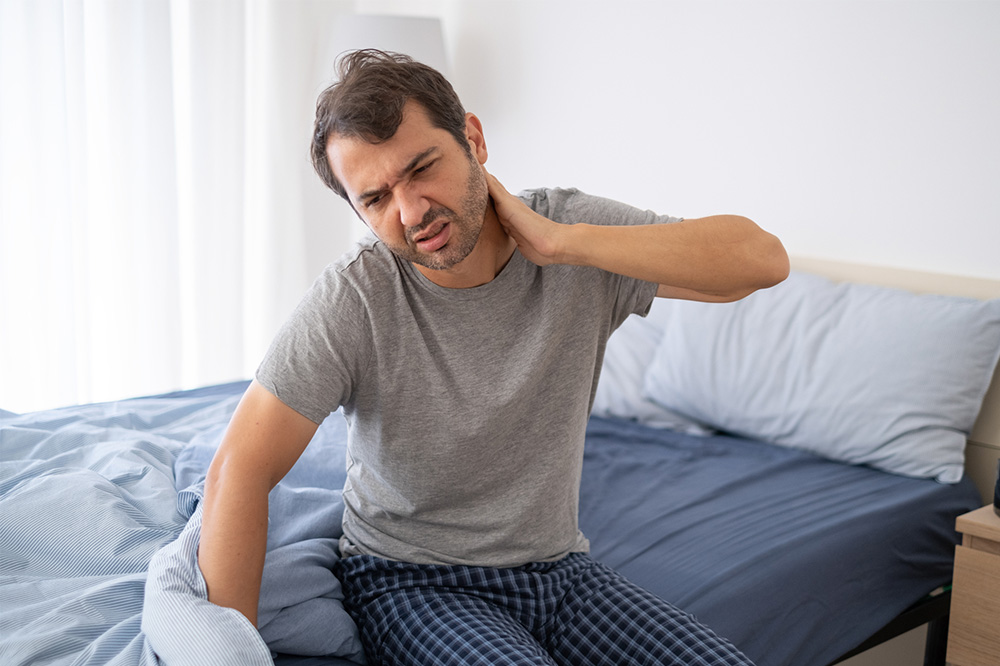 Man suffering from neck pain while waking up.
