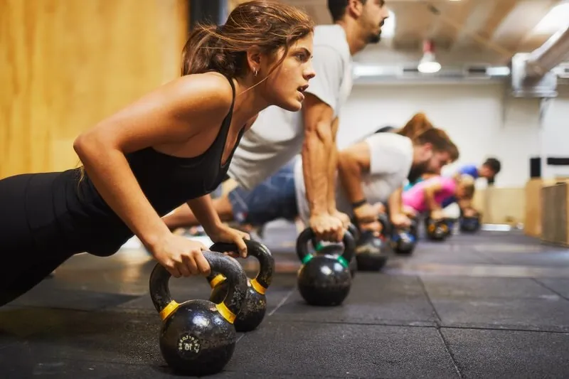 Group fitness class performing pushups with dumbells.