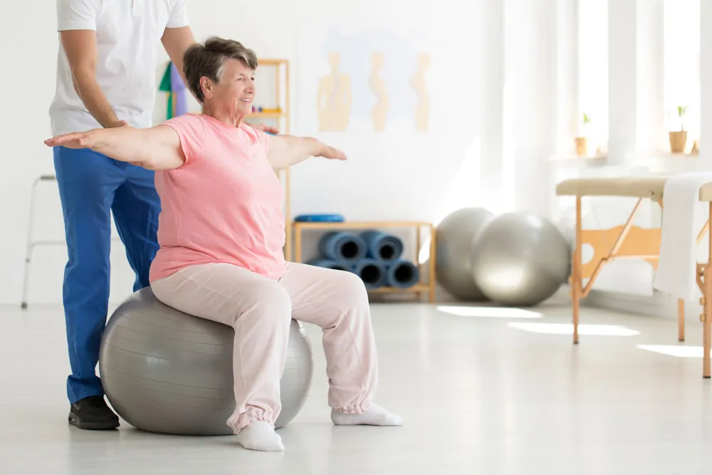 Older woman sitting on fitness ball, stretching hands trying to balance.