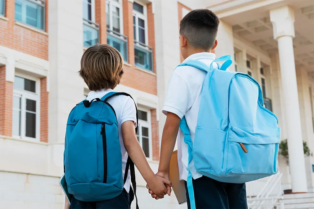 Two boys wearing school backpacks properly.