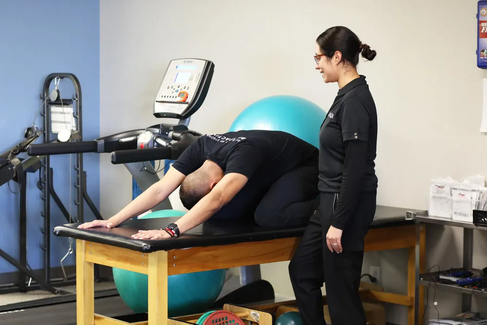 Therapist helping patient perform child pose stretch to improve posture.