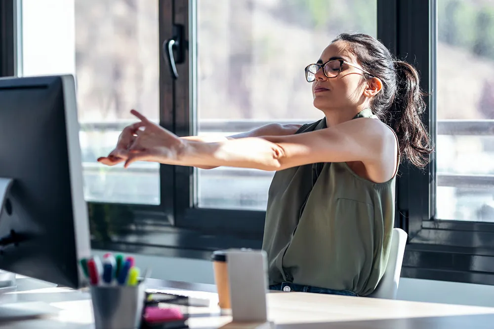 Woman stretching at desk to refresh poor posture.