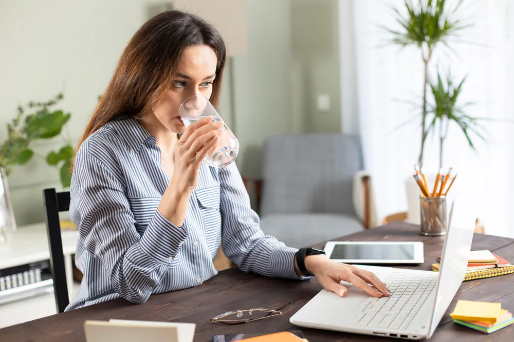 woman drinking water while working on computer