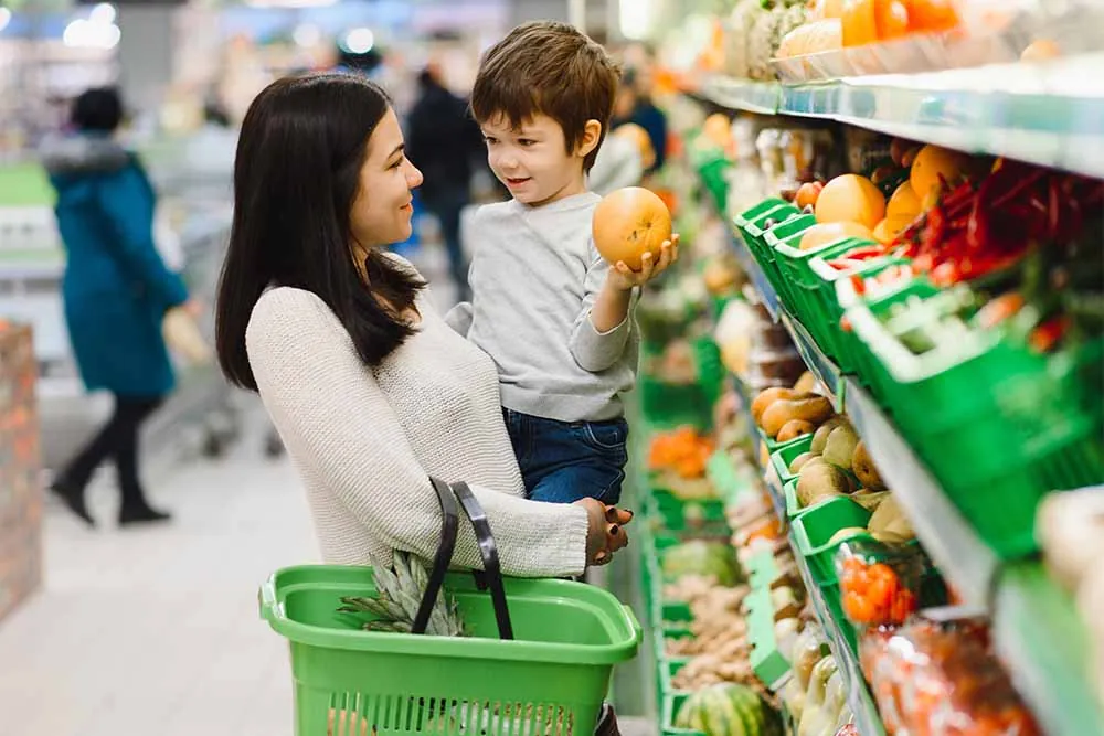 Boy helping mom choose fruit in grocery store.