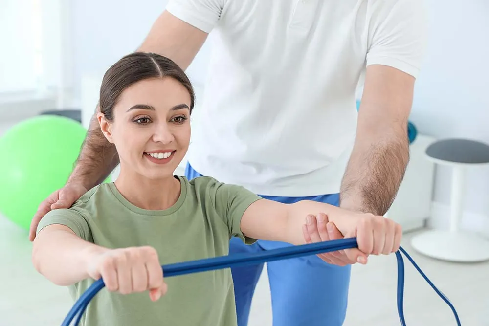 Physical therapist assisting woman with arm resistance band exercise.